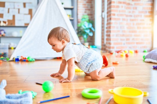 Adorable toddler crawling around lots of toys at kindergarten