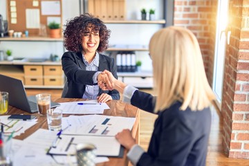 Two beautiful bussineswomen smiling happy. Working together shaking hands for agreement at the office