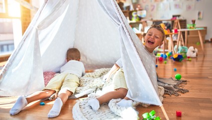 Adorable blonde twins playing inside tipi around lots of toys at kindergarten