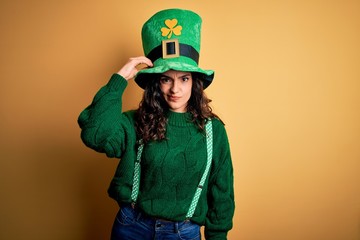Beautiful curly hair woman wearing green hat with clover celebrating saint patricks day confuse and wonder about question. Uncertain with doubt, thinking with hand on head. Pensive concept.