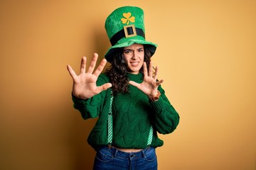 Beautiful curly hair woman wearing green hat with clover celebrating saint patricks day afraid and terrified with fear expression stop gesture with hands, shouting in shock. Panic concept.
