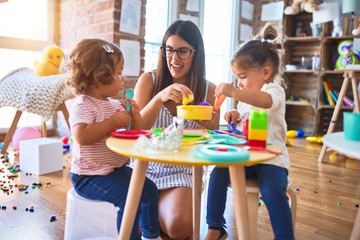 Young beautiful teacher and toddlers playing meals using plastic food and cutlery toy at...