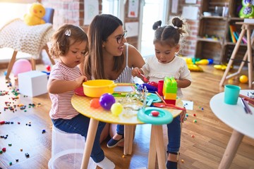 Young beautiful teacher and toddlers playing meals using plastic food and cutlery toy at kindergarten