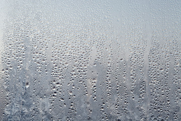 Frozen drops of condensed steam water drops on the transparent window glass. Clean background. Condensation of moisture at extreme temperatures. Water vapor condenses on cold window glass and freezes