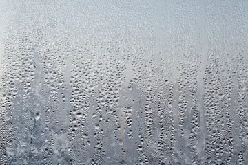 Poster Frozen drops of condensed steam water drops on the transparent window glass. Clean background. Condensation of moisture at extreme temperatures. Water vapor condenses on cold window glass and freezes © Aleksandr