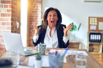 Middle age beautiful businesswoman working using laptop at the office celebrating crazy and amazed for success with arms raised and open eyes screaming excited. Winner concept