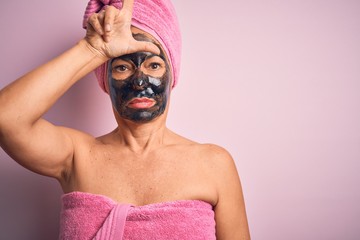 Middle age brunette woman wearing beauty black face mask over isolated pink background making fun of people with fingers on forehead doing loser gesture mocking and insulting.