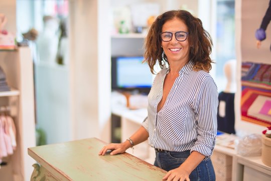 Middle age beautiful clothes shop owner woman smiling happy and confident waiting customers at counter