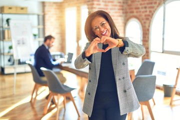 Middle age beautiful businesswoman wearing jacket and glasses standing at the office smiling in...