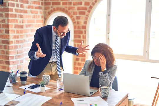 Two middle age business workers working together. Man bullying woman at the office
