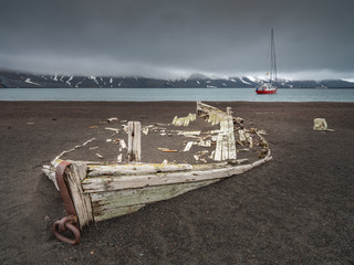 view to ruins of old wooden boat and red yacht at the sea