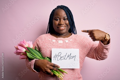 Plus size african american woman holding best mom message and tulips on mothers day with surprise face pointing finger to himself