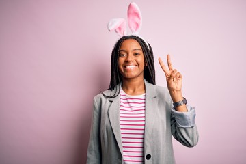 Young african american girl wearing cute easter bunny ears over pink background smiling with happy...