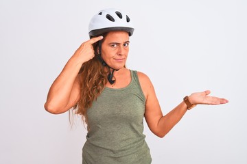 Middle age mature cyclist woman wearing safety helmet over isolated background confused and annoyed with open palm showing copy space and pointing finger to forehead. Think about it.