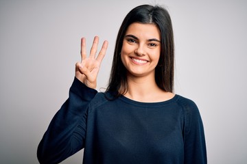 Young beautiful brunette woman wearing casual sweater standing over white background showing and pointing up with fingers number three while smiling confident and happy.