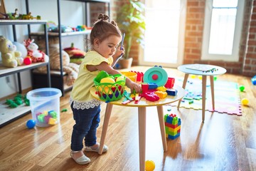 Beautiful toddler playing on the table with plastic vegetables and dishes at kindergarten