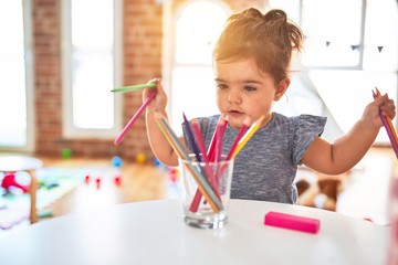 Beautiful toddler standing holding colored pencils at kindergarten