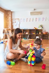 Young beautiful teacher and toddler playing with building blocks toy at kindergarten