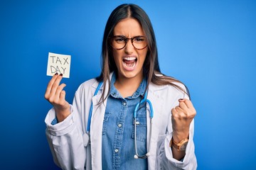 Young doctor woman wearing stethoscope holding paper with tax day message annoyed and frustrated shouting with anger, crazy and yelling with raised hand, anger concept