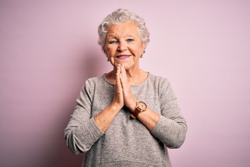 Senior beautiful woman wearing casual t-shirt standing over isolated pink background praying with hands together asking for forgiveness smiling confident. - obrazy, fototapety, plakaty