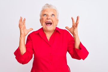 Senior grey-haired woman wearing red casual shirt standing over isolated white background crazy and...