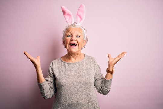 Senior beautiful woman wearing bunny ears standing over isolated pink background celebrating crazy and amazed for success with arms raised and open eyes screaming excited. Winner concept