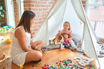 Beautiful teacher and blond toddler girl playing with dolls inside tipi at kindergarten