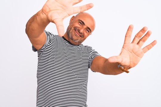Middle age handsome man wearing striped navy t-shirt over isolated white background doing frame using hands palms and fingers, camera perspective