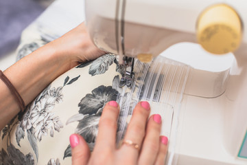 Process of sewing the curtains at home, close up of curtain tape on the sewing machine, hemming, tailoring, repairing and stitching cloth and dress, with the hand of female dressmaker in background