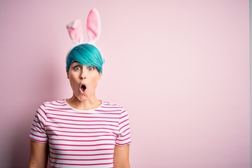 Young woman with fashion blue hair wearing easter rabbit ears over pink background afraid and shocked with surprise expression, fear and excited face.