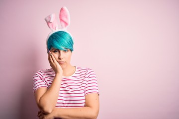 Young woman with fashion blue hair wearing easter rabbit ears over pink background thinking looking tired and bored with depression problems with crossed arms.