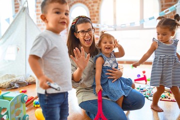 Beautiful teacher and group of toddlers playing around lots of toys at kindergarten