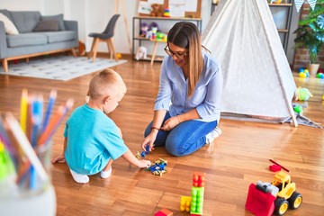 Young caucasian child playing at playschool with teacher. Playing with toy soldiers at playroom around toys.