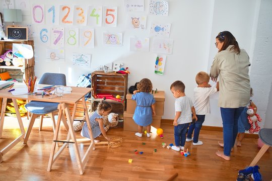 Beautiful teacher and group of toddlers playing around lots of toys at kindergarten