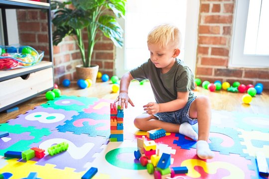 Young caucasian kid playing at kindergarten with toys. Preschooler boy happy at playroom.