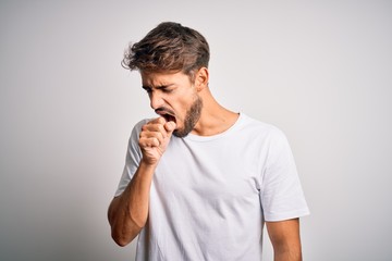 Young handsome man with beard wearing casual t-shirt standing over white background feeling unwell and coughing as symptom for cold or bronchitis. Health care concept.