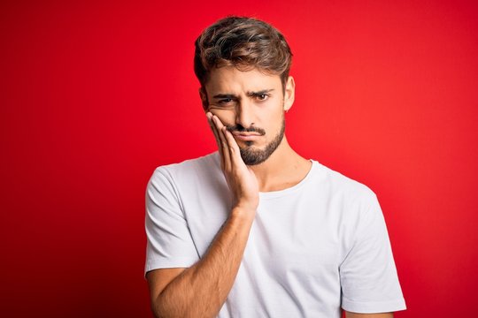 Young handsome man with beard wearing casual t-shirt standing over red background thinking looking tired and bored with depression problems with crossed arms.
