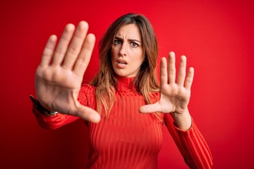 Young beautiful brunette woman wearing casual turtleneck sweater over red background doing stop gesture with hands palms, angry and frustration expression