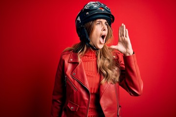 Young beautiful brunette motrocyclist woman wearing moto helmet over red background shouting and screaming loud to side with hand on mouth. Communication concept.