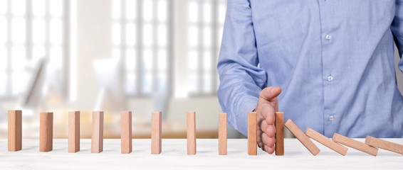 businessman stopping falling wooden blocks with his hand. domino effect intervention concept
