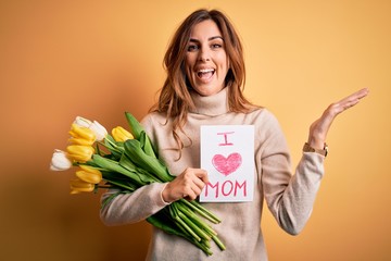 Beautiful brunette woman holding love mom message and tulips celebrating mothers day very happy and excited, winner expression celebrating victory screaming with big smile and raised hands