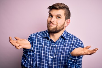 Young handsome blond man with beard and blue eyes wearing casual shirt standing clueless and...