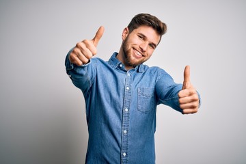 Young handsome blond man with beard and blue eyes wearing casual denim shirt approving doing positive gesture with hand, thumbs up smiling and happy for success. Winner gesture.