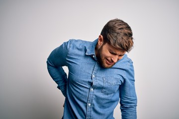 Young handsome blond man with beard and blue eyes wearing casual denim shirt Suffering of backache, touching back with hand, muscular pain