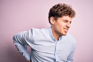 Young blond handsome man with curly hair wearing striped shirt over white background Suffering of backache, touching back with hand, muscular pain