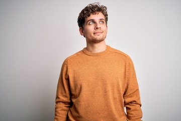 Young blond handsome man with curly hair wearing casual sweater over white background smiling looking to the side and staring away thinking.