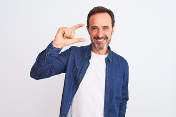 Middle age handsome man wearing blue denim shirt standing over isolated white background smiling and confident gesturing with hand doing small size sign with fingers looking and the camera