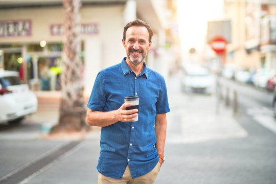 Middle age handsome man standing on the street drinking take away coffee smiling