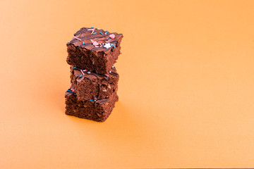 Chocolate brownie dessert with almond nut, chocolate glaze on an orange background.
