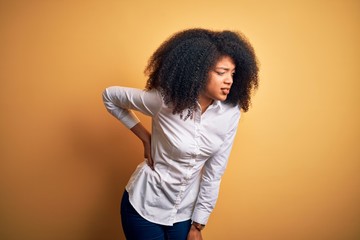 Young beautiful african american elegant woman with afro hair standing over yellow background Suffering of backache, touching back with hand, muscular pain